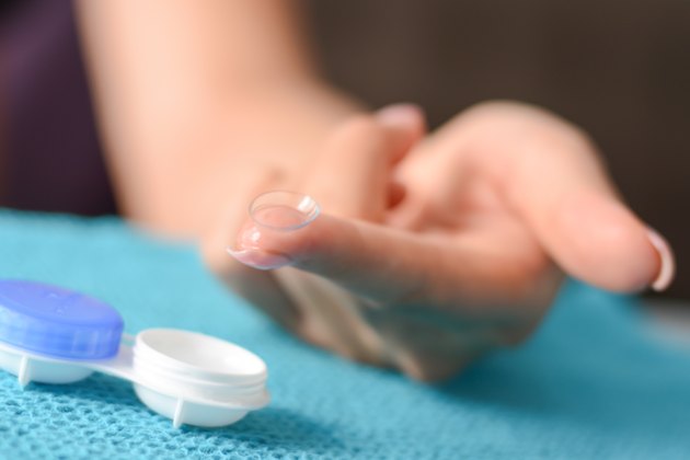 Soft contact lens on woman's fingertip with open case