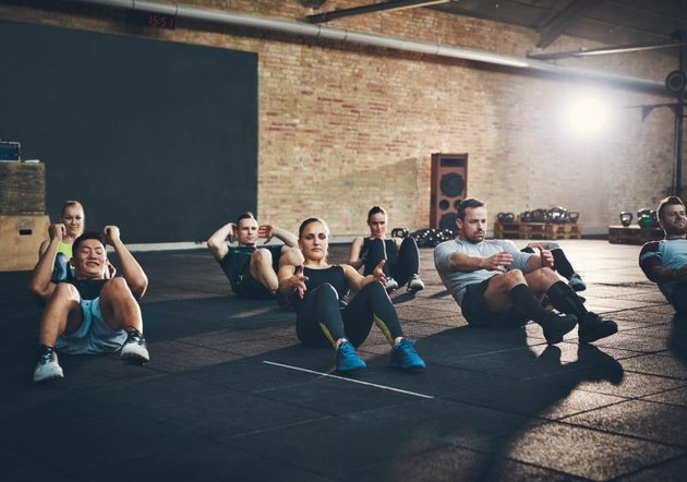 Group of athletic adult men and women performing sit up exercises to strengthen their core abdominal muscles at fitness training