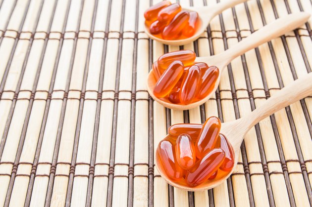Fish oil capsules in wooden spoon on bamboo mat