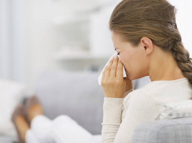 young woman laying on sofa and blowing nose