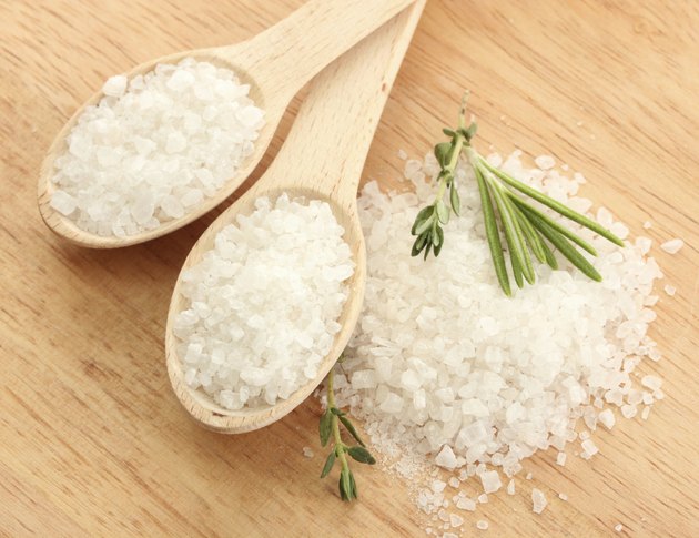 salt in spoons with fresh rosemary and thyme on table