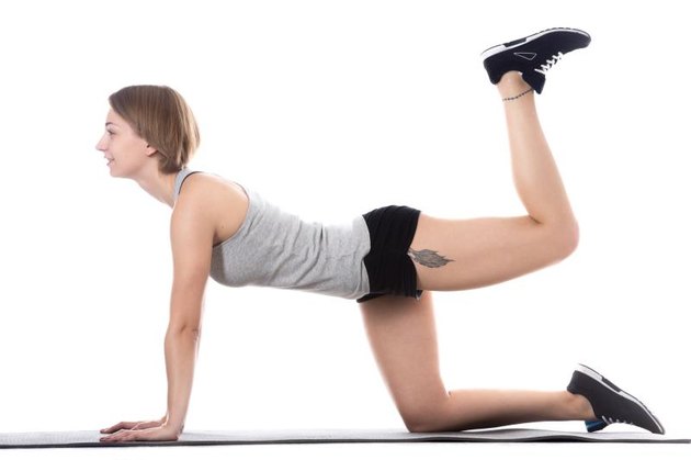 Young cheerful sporty attractive woman doing fitness training, exercises for hips and butt on mat, full length isolated studio image on white background