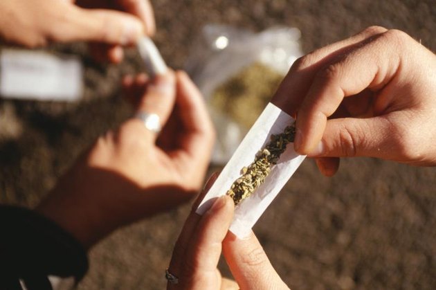 People rolling joints on street, closeup of hands.