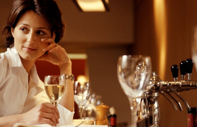 Woman sitting at table in restaurant, holding glass of wine, close-up