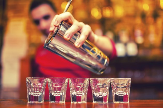 barman pouring cocktail drinks into shot glasses
