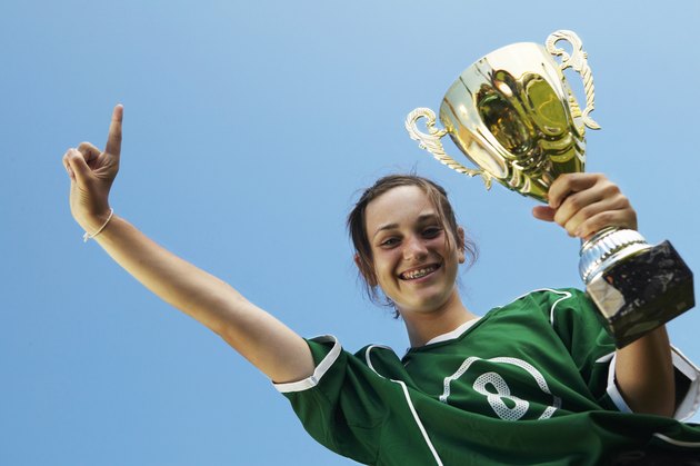 Female (11-13) footballer with trophy, other hand raised, smiling