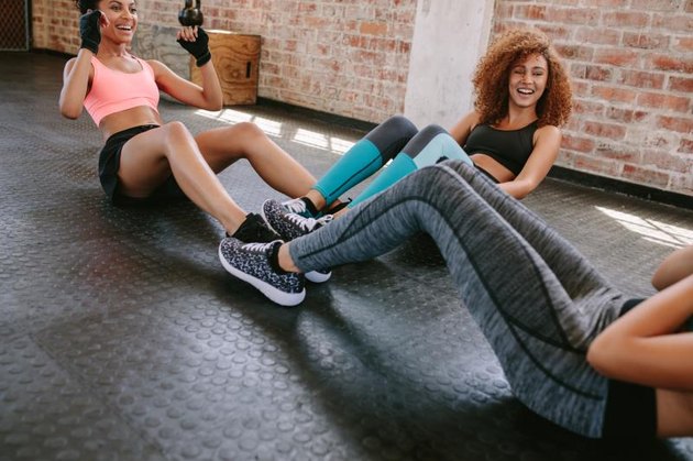 Group of female exercising in healthclub. Three young woman doing situps together in gym.