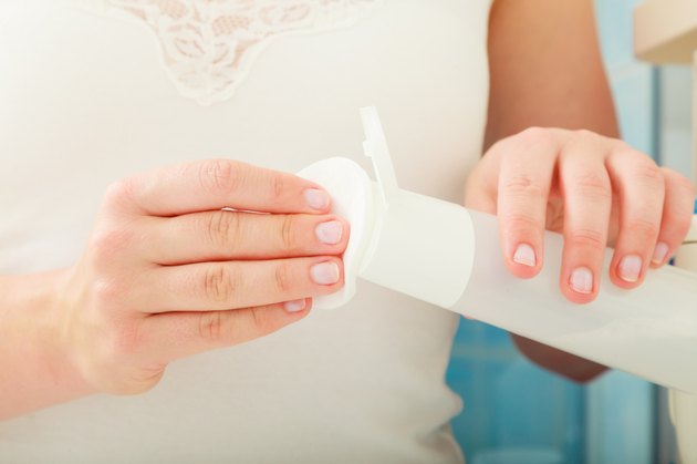 woman holding cotton swab and makeup remover in hands