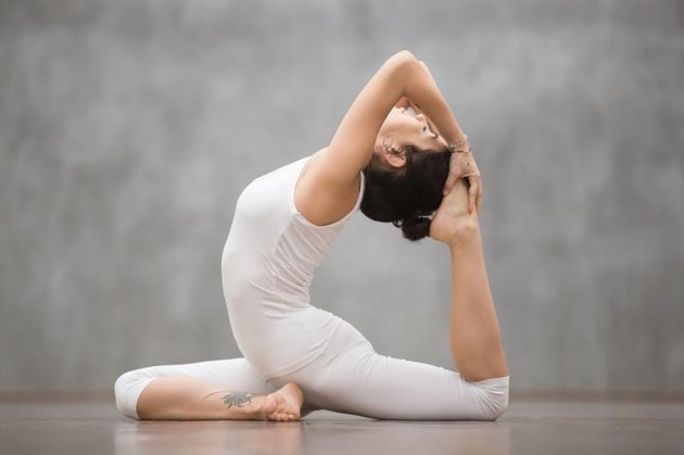 Side view portrait of beautiful young woman wearing white sportswear working out in fitness club or at home, doing yoga or pilates exercise. One Legged King Pigeon pose, Eka Pada Rajakapotasana
