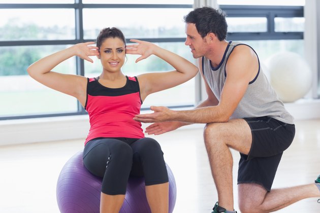 Trainer helping woman do abdominal crunches on fitness ball