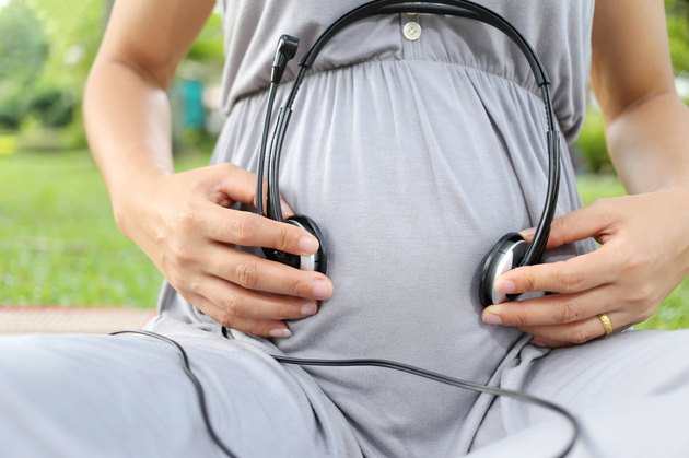 Pregnant women put earphone in hand on her belly.