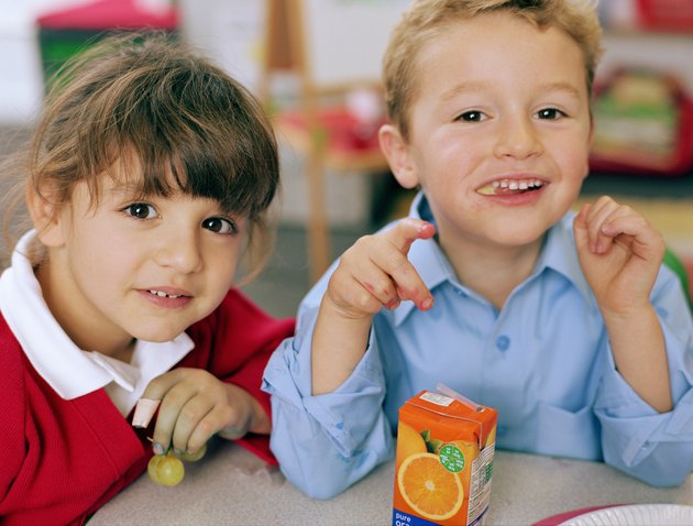 Schoolgirl and boy (4-6) at table, smiling, close-up, portrait