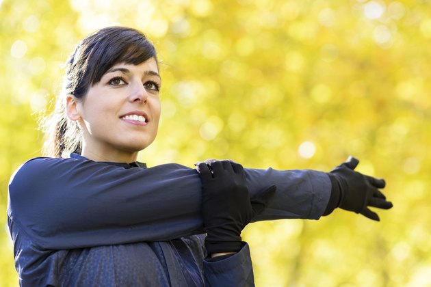 Beautiful sportswoman stretching shoulder and arm outdoors