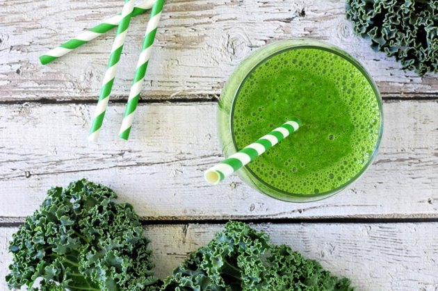 Green kale smoothie overhead view, in a glass with straw on an aged wood background