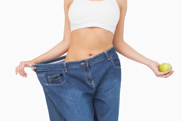 Mid section of slim woman wearing too big jeans holding an apple