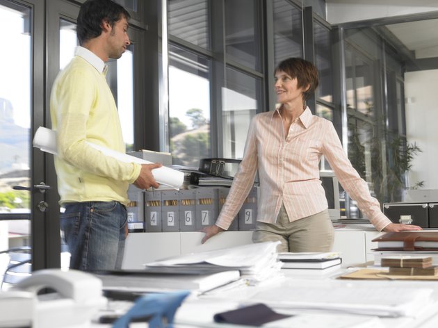 Businesswoman and man in office talking, man holding plans