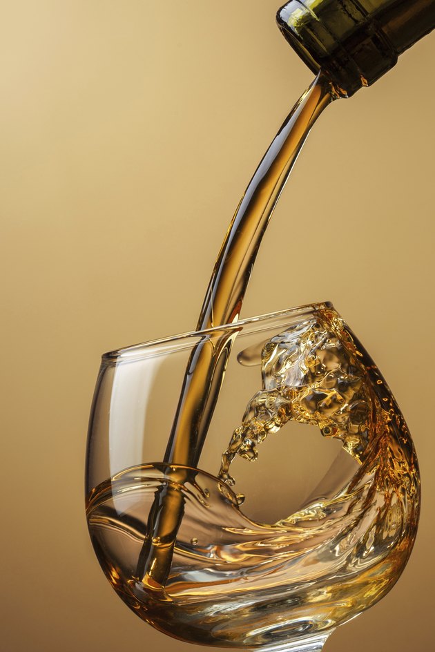 Cognac pouring from bottle into glass with splash on brown