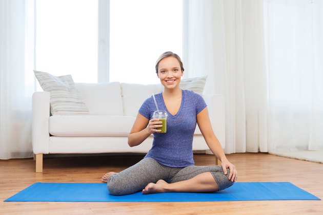 happy woman with smoothie sitting on mat at home