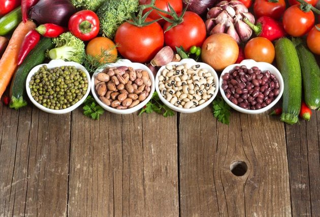 Legumes in bowls and vegetables on a wooden table