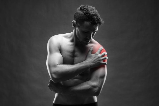 Pain in the shoulder. Muscular male body. Handsome bodybuilder posing on gray background. Black and white photo with red dot