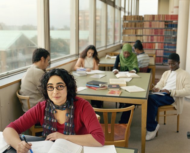 Students at tables in library work space, woman smiling, portrait