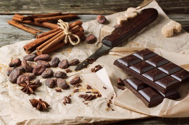 Dark chocolate with knife, cocoa beans, cinnamon and anise on crumpled paper over wooden background
