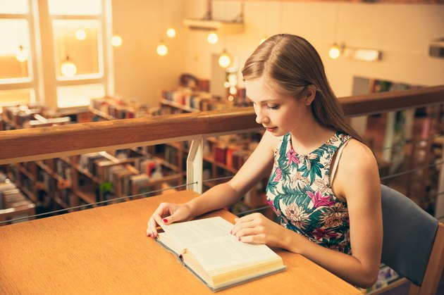 Beautiful young woman student in library reading a book