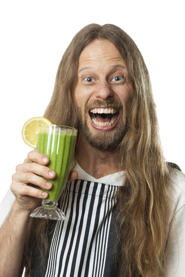 Happy hippie drinking green vegetable smoothie on white