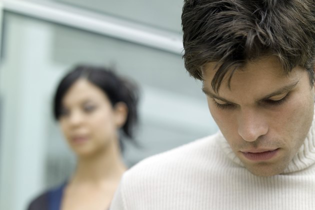 Young man looking down and a young woman behind him