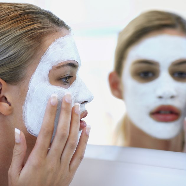 Young woman putting on face pack, reflection in mirror