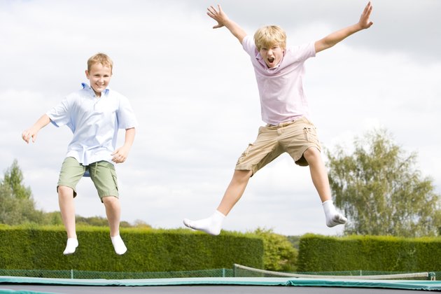 Two young boys jumping on trampoline smiling