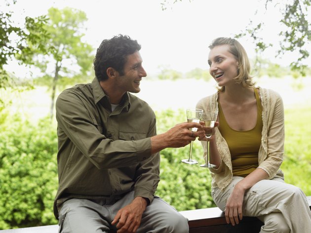 Couple sitting on balcony toasting each other with drinks, smiling