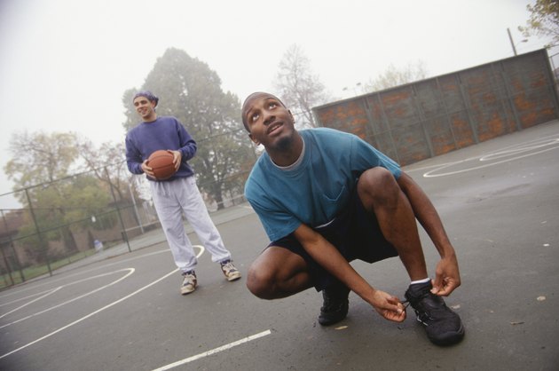 Young man lacing up basketball shoes on street court