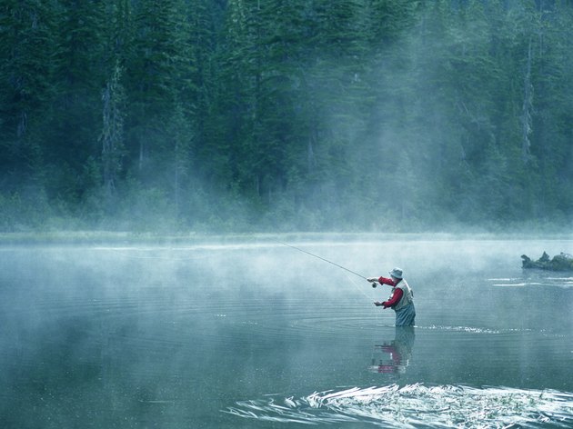Senior fly fisherman standing in lake covered with fog, casting line