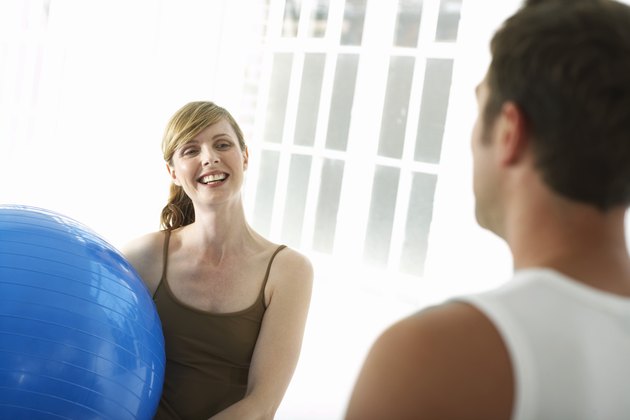 Woman holding exercise ball, smiling at man
