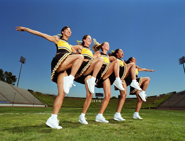 Cheerleaders dancing arm and arm in formation, lifting knee, low angle