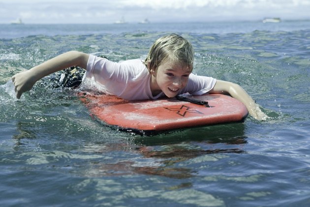 Boy (12-13), lying on bodyboard in ocean
