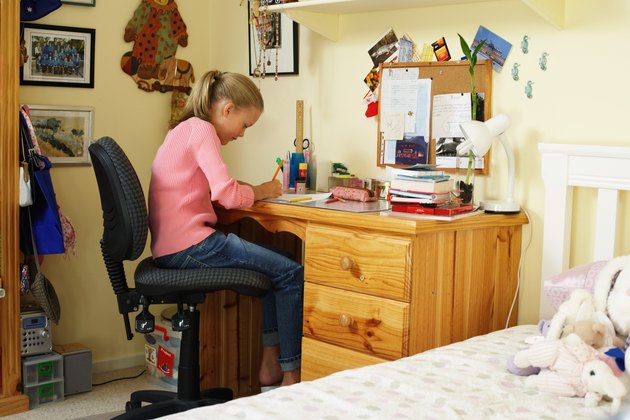 Girl (10-12) doing homework at desk in bedroom, side view