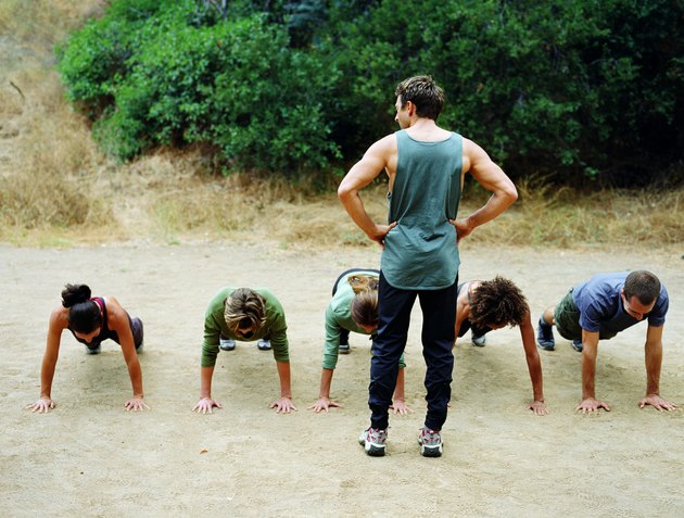 Man standing over group of people doing pushups, rear view