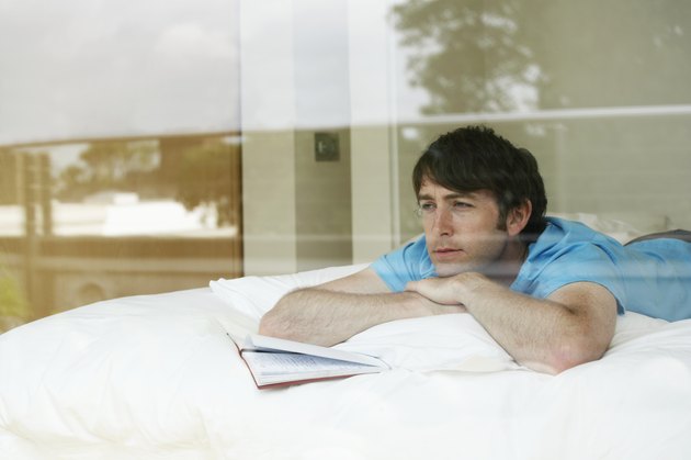 Young man lying on bed with open diary, view through window