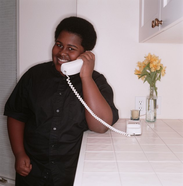 Teenage boy (16-17), talking on telephone in home, portrait