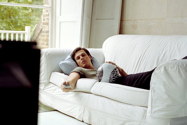 Man lying on sofa using television remote control
