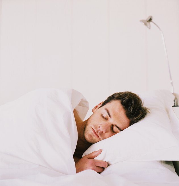 Young man sleeping with duvet covering him in bed