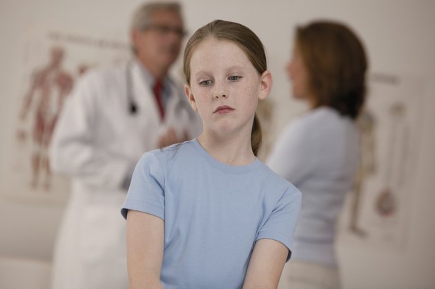 Sick girl sitting in doctor's office while mother and doctor talk in background