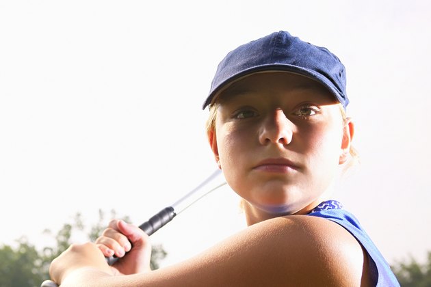 A softball player looking over her shoulder preparing to hit the ball