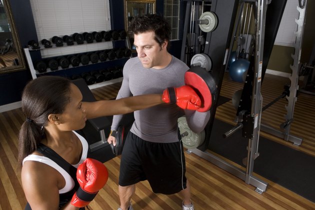 Trainer instructing a young woman with boxing equipment in the gym