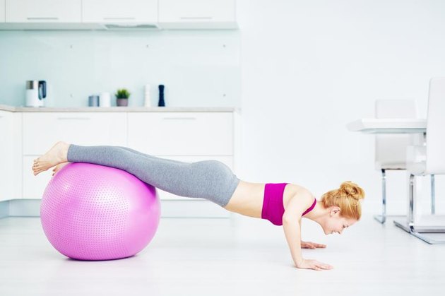 Girl doing push-ups in the kitchen with her legs on fitball