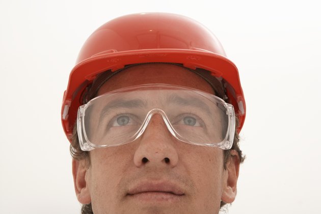 Man wearing protective eyewear and hard hat, looking up
