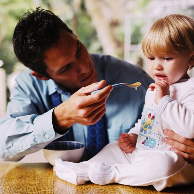 a young man feeding his daughter (1-3) on the table