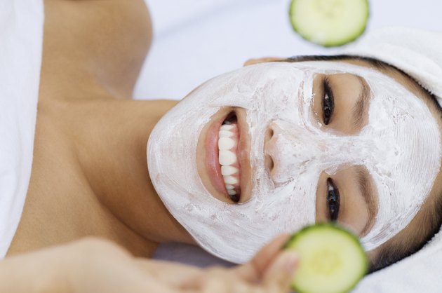 Young woman having facial treatment, holding cucumbers, portrait
